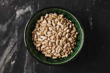 Raw sunflower seeds in bowl. Healthy vegetarian snack. Natural peeled seeds on black marble table. Top view food concept. Organic ingredient rich in fiber. Rustic oriental kitchen background.