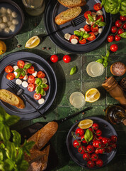 Caprese salad with tomatoes, mozzarella, basil, and baguette on green tiles
