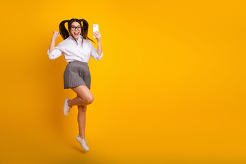 Cheerful young female student smiling while holding a smartphone, excited expression against a...