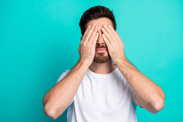 Young man covering his eyes with hands on a teal background, expressing playfulness and curiosity...