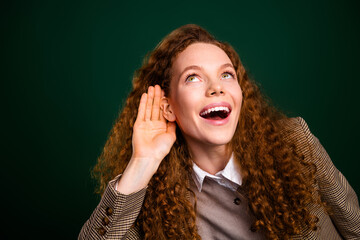 Confident young businesswoman with curly hair showcasing a listening gesture on an emerald green...