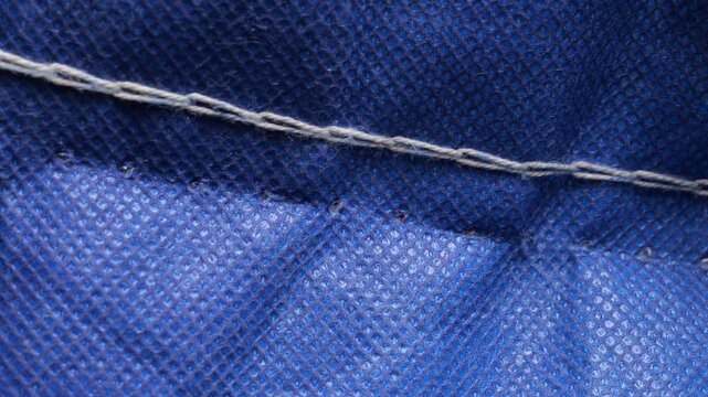 Precise handheld seam ripper carefully detaching white stitches from vibrant blue fabric, capturing delicate process of garment alteration in crisp slow motion