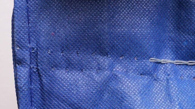 Close-up slow motion of a seamstress using a seam ripper to remove stitches from a piece of blue fabric