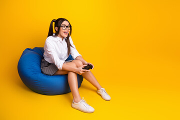 Smiling young woman holding a gaming controller while sitting on a blue beanbag chair against a...