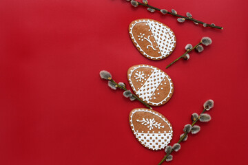 Romantic decorated Easter gingerbread cookies in a shape of egg, with willow twigs, red background, copy space for text