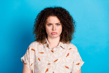 Portrait of a young woman expressing discontent on a blue background, showcasing casual style and a...