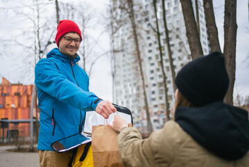 Smiling delivery man handing over a paper bag filled with takeaway food to a customer on a bustling city street, surrounded by buildings and trees in the vibrant urban landscape