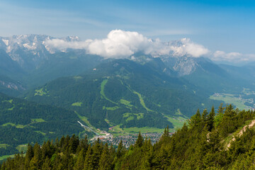 Hiking above the clouds on Wankberg, Germany—panoramic views of snow-capped Alps and lush valleys under a bright blue sky.