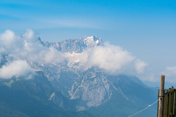 Hiking above the clouds on Wankberg, Germany—panoramic views of snow-capped Alps and lush valleys under a bright blue sky.