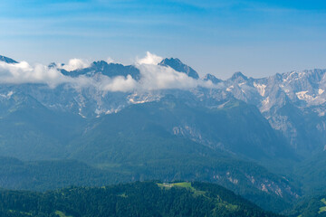 Hiking above the clouds on Wankberg, Germany—panoramic views of snow-capped Alps and lush valleys under a bright blue sky.