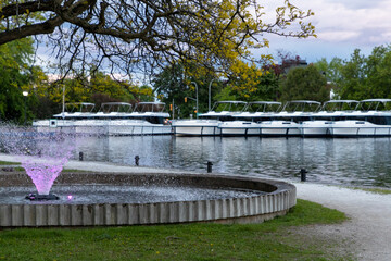 Park with lighted fountains along Rideau River with boats in Smiths Falls town in Ontario, Canada in spring season during sunset. Centennial Park