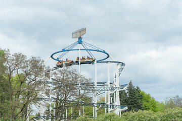 Thrilling Amusement Park Ride Soaring Above Lush Green Trees Under A Bright Sky. Exciting Adventure...