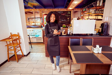 African American waitress in a cozy cafe holding a tablet and smiling