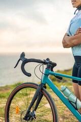 Obraz premium vertical Latin cyclist woman posing with gravel bike at sunrise by the sea