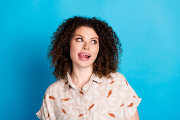 Cheerful young woman with curly brown hair making a playful face against a light blue background...