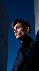 Fashionable Male Model in Dark Coat Posing Outdoors Against Blue Sky