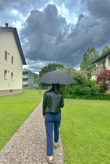 young woman walking under umbrella in rainy weather with grey dark clouds


