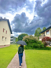 young woman walking under umbrella in rainy weather with grey dark clouds

