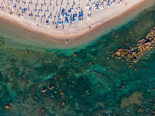High-angle drone photograph of a beautiful sandy beach lined with white sunbeds and blue umbrellas....