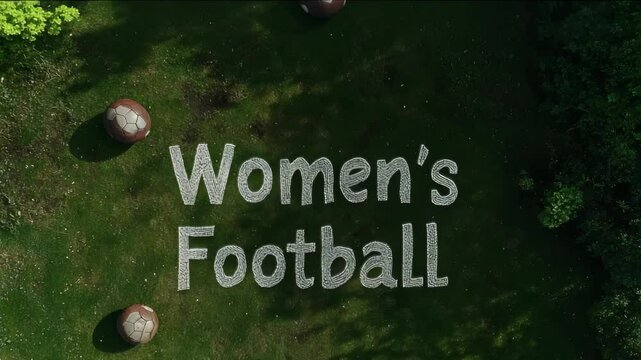 A soccer ball is on the grass next to a sign that says Women's Football. The sign is made of yellow letters and is surrounded by grass