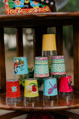 Stacked, decorated glasses on a wooden shelf. Colorful and unique designs adorn the glass. Perfect for a playful and whimsical gathering.