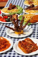 table with meat and pasta dishes and cooked lasagna and skewers