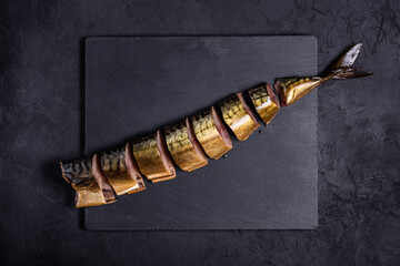 sliced ​​cold smoked mackerel without head lies diagonally on stone cutting board on black background. top view. seafood concept with copy space