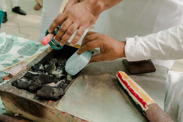 Crafting with fire and chalk: A person in white melts and molds vibrant materials over charcoal in an artistic process.
