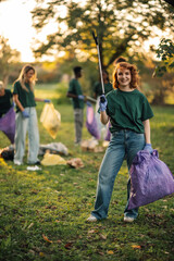 Young volunteer smiling and posing while picking up trash in a park
