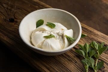 Whole tied Italian cheese burrata on small wooden cutting board served with fresh oregano