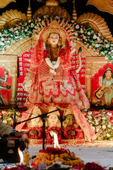 Obraz premium Elaborate statue of deity, adorned in red & gold. Floral arrangement & flame accents enhance the worshipful ambience. Sacred art