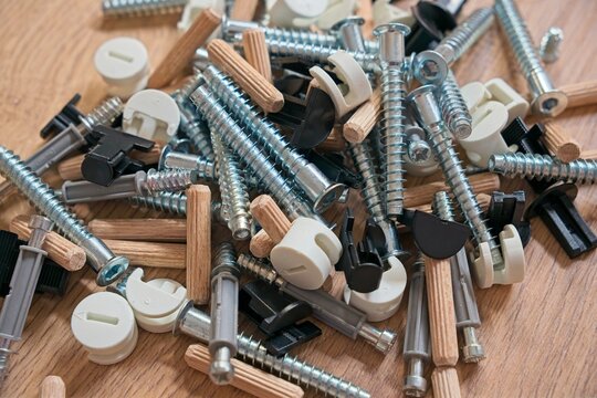 Wooden workbench displaying scattered hardware - metal screws, wooden dowels, plastic connectors for furniture assembly and home repair