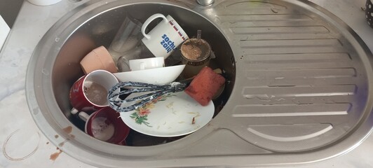 Dirty dishes piled up in stainless steel kitchen sink, top view