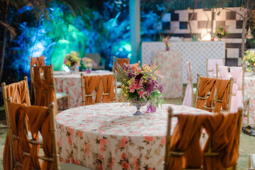 Elegant dining setup with floral arrangements, draped chairs, and patterned tablecloths for a special event. Soft lighting enhances the ambiance.