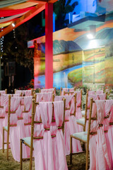 Elegant wedding ceremony setup with pink draped chairs and a colorful backdrop featuring a painted landscape scene, creating a romantic atmosphere.