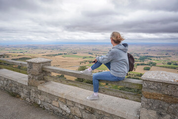 Young woman wearing jeans and a gray sweatshirt contemplating the landscape of the province of Burgos on a cloudy day from a viewpoint