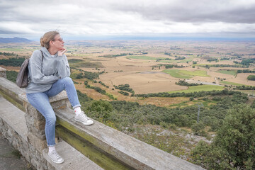 Young woman wearing jeans and a gray sweatshirt contemplating the landscape of the province of Burgos on a cloudy day from a viewpoint