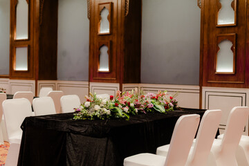 Elegant event setup with floral centerpiece and covered chairs, creating a formal atmosphere for a special occasion. Classic and sophisticated decor.