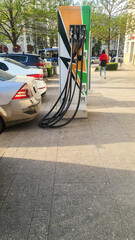 A busy gas station with multiple cars parked. Fuel pumps are visible, Trees line the street.