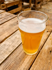 Glass of light amber beer on wooden table outdoors, casual beverage concept.