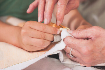 Close-up of child and grandmother sewing together with joined hands