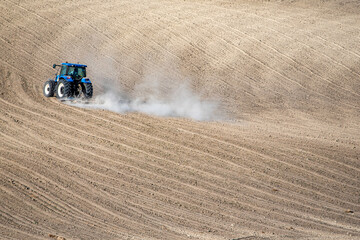 A tractor moves across freshly plowed wavy soil, highlighting agricultural machinery and rural productivity in a minimalist landscape