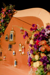 Ornate lanterns hang in an elegant arrangement. A frame is covered in colorful flowers, creating a warm and inviting atmosphere.