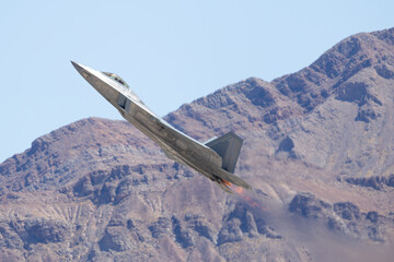 Side view of a  F-22 Raptor  in a climb against the Nevada hills, with afterburners on.