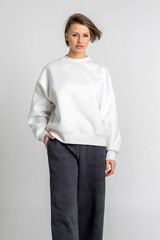 Portrait beautiful woman of model appearance. Girl in white sweatshirt, black trousers, on grey background. Pretty female with trendy makeup posing in studio. Vertical photo.