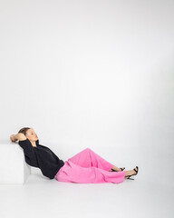 Portrait beautiful woman of model appearance. Girl in black jumper and pink trousers on grey background. Pretty female with trendy makeup posing in studio. Vertical photo. 