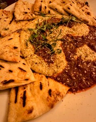 Vertical image of flatbread with hummus and chilli sauce