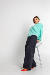 Portrait beautiful woman of model appearance. Girl in mint jumper, black trousers, red shoes on grey background. Pretty female with trendy makeup posing in studio. Vertical photo.