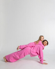 Young mother and little daughter walking holding hands. Dressed in pink color suits on white background, studio. Concept of advertising positive and clothes. Vertical photo