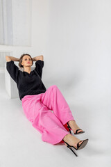 Portrait beautiful woman of model appearance. Girl in black jumper and pink trousers on grey background. Pretty female with trendy makeup posing in studio. Vertical photo. 